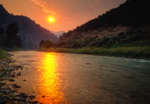 Forest Fire Sunset Colorado River - Scenic river landscape with dramatic warm sunset light from forest fires and smoke in atmosphere.