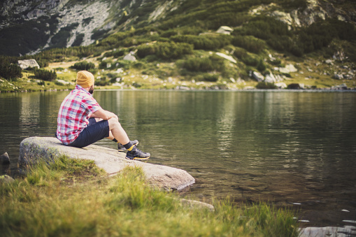 Traveler sits alone on a rock and enjoying the view of lake in mountains