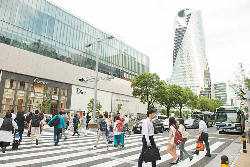 Nagoya, Japan - May 31, 2016: Near the Nagoya Station many Japanese people cross the street at the crosswalk as they walk to their destinations in the afternoon rush hour. Modern buildings and luxury stores are visible in the background as traffic waits for the light to change.