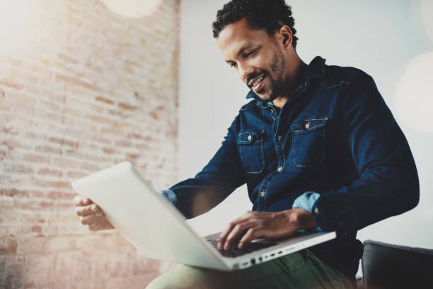 istock Smiling young African man using laptop while sitting at his 638559518