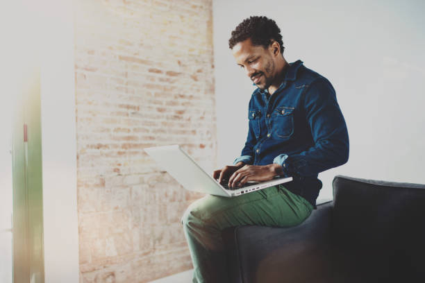 istock Smiling young African man working with laptop while sitting on 638559640