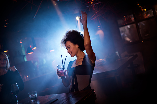 Woman in the club dancing and having a cocktail at her night out.