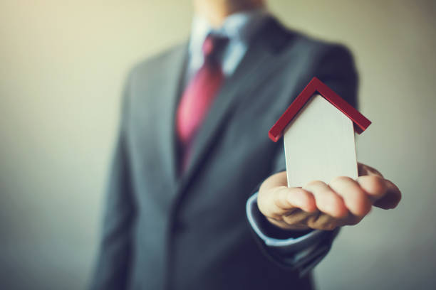Business man in suit having miniature house on palm of his hand - Business mortgage, property loan, house insurance, business investment concept.