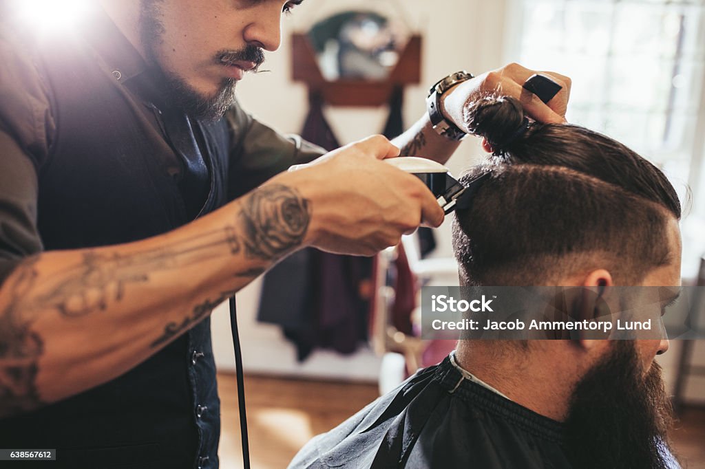 Man getting trendy haircut in barber shop Close up shot of man getting trendy haircut at barber shop. Male hairstylist serving client, making haircut using machine and comb. Cutting Hair Stock Photo