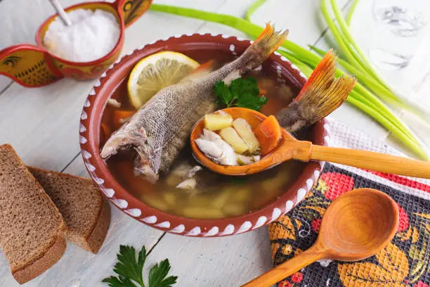 Traditional Russian fish soup in a clay bowl on a wooden table. Rustic style