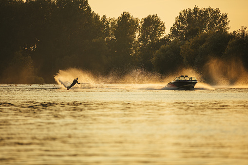 Outdoor shot of man wakeboarding on lake at sunset. Water skiing on lake behind a boat.