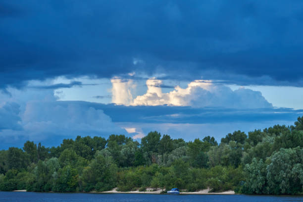 Landscape. The sandy coast of the river overgrown with deciduous forest. In the sky cumulonimbus