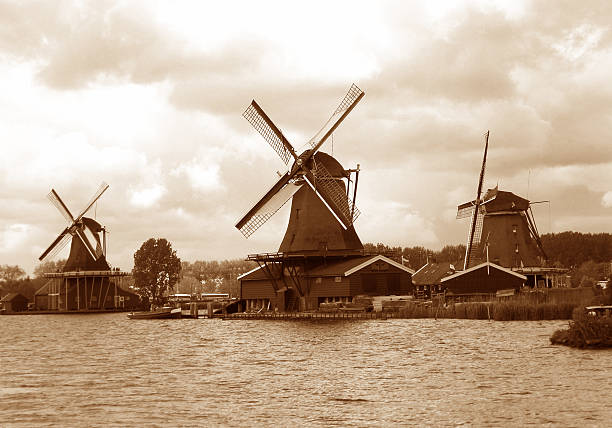 Sepia tone of three waterfront Dutch windmills under the cloudy sky, Zaanse Schans, Netherlands