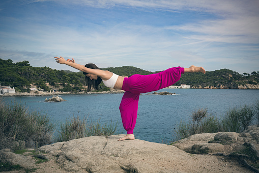 Young woman doing yoga at the sea Warrior 3 pose