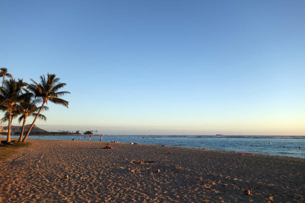 People hang out at Ala Moana Beach Park at Dusk with iconic Diamondhead in the distance during a beautiful day on the island of Oahu, Hawaii.