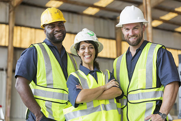Construction crew with female boss Three multi-ethnic workers wearing hardhats and safety vests. The foreman is the Hispanic woman standing in the middle with her arms crossed, smiling confidently at the camera. reflective clothing photos stock pictures, royalty-free photos & images