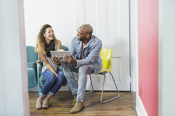 デジタルタブレットを見て、話している2人の若者 - talking chair two people sitting ストックフォトと画像