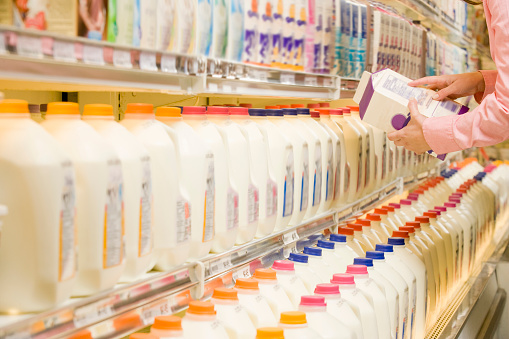 Mujer comprobando los ingredientes en la parte posterior del cartón de leche en el supermercado photo
