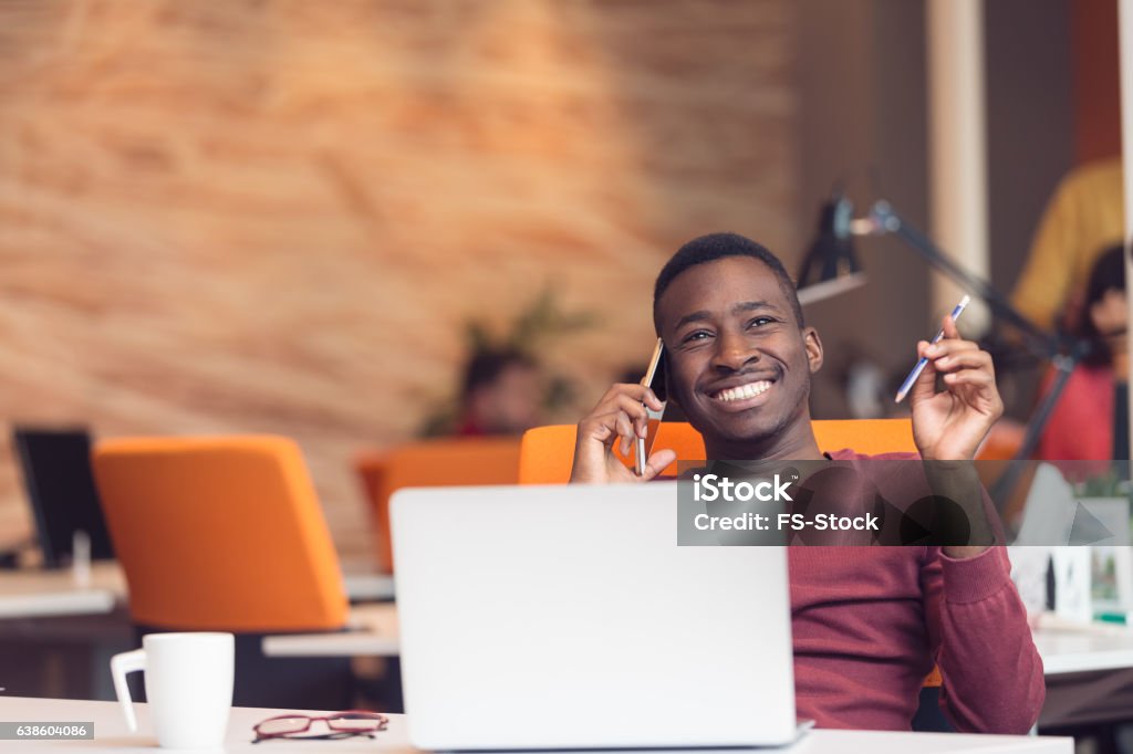 African American businessman sitting at the computer in startup office African American businessman on the phone sitting at the computer in his startup office Business Stock Photo