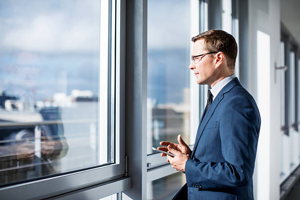 uomo d'affari maturo in piedi vicino alla finestra in ufficio - side window foto e immagini stock