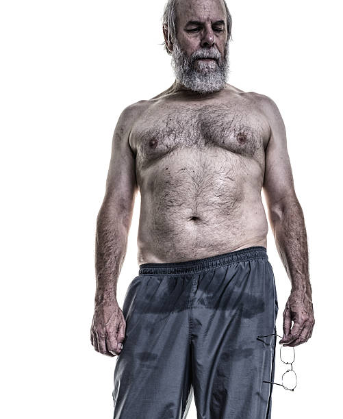 Real Body Senior Adult Man Sweating After Gym Workout A shirtless, real person, real body - with warts, bruises, blemishes and all, senior adult man is tired mentally and physically exhausted. His workout pants are drenched - he is resting, but still sweating heavily after a vigorous gym exercise workout. He remains somewhat overweight, but following a rigorous fitness improvement routine seriously for several years  has made him more muscular and much more fit overall. He is determined to continue. His goal is to get stronger and stay fit for life. fat guy no shirt stock pictures, royalty-free photos & images
