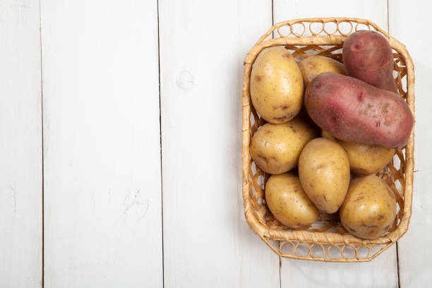 Raw potatoes with burlap on white wooden background, top view