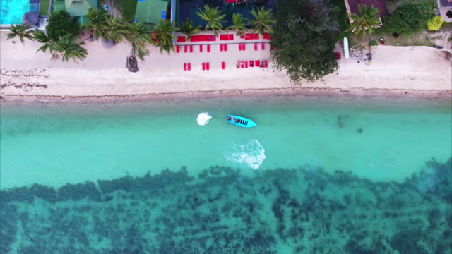 Aerial shot of a Boat leaving the beach by a resort in the tropics