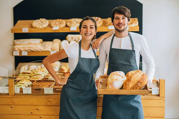 Two beautiful young bakers holding bread at the bakery.
