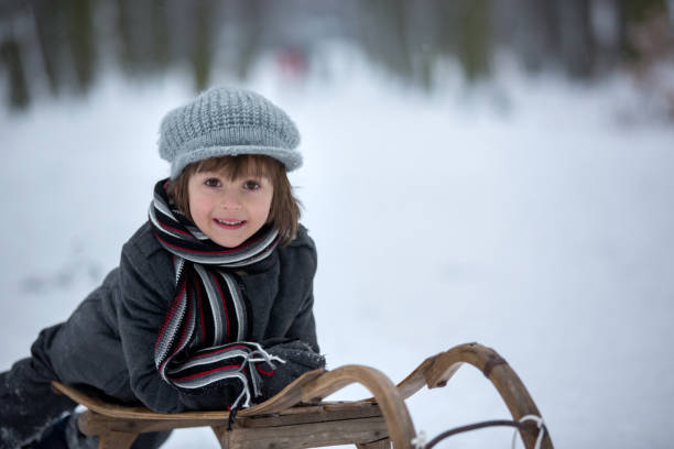 netter kleiner junge, auf schlitten liegend, lächelnd in die kamera - little boys sled clothing slide stock-fotos und bilder