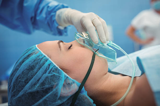 хирург регулировки кислородной маски на рот пациента в театре операции - operative стоковые фото и изображения