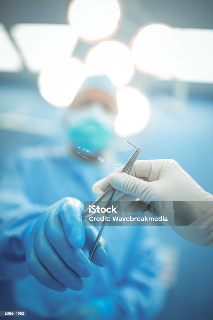 Surgeon passing surgical tool to colleague in operation theater Surgeon passing surgical tool to colleague in operation theater at hospital Surgeon Stock Photo