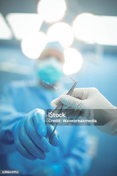Surgeon Passing Surgical Tool To Colleague In Operation Theater Stock Photo - Download Image Now