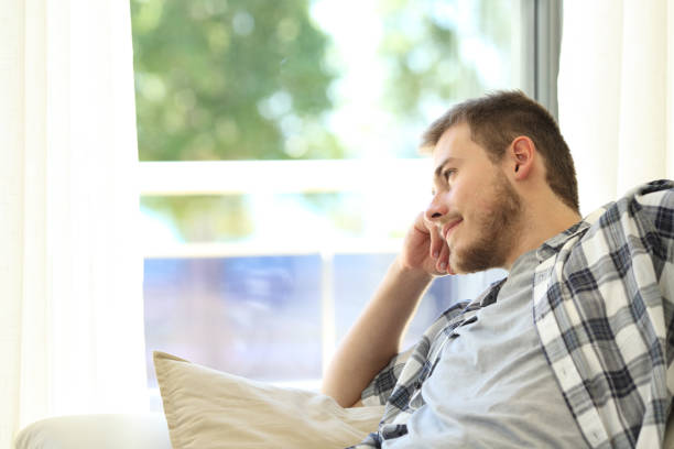 istock Man sitting on a couch and looking through a window 638647402