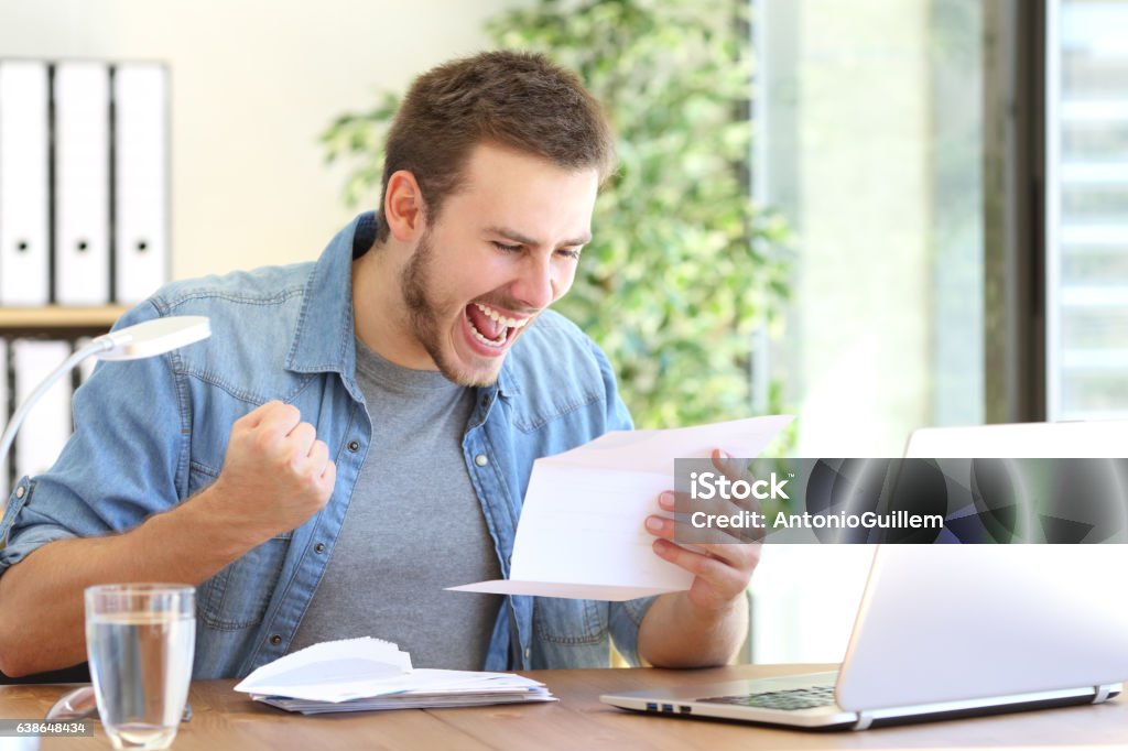 Excited entrepreneur reading a letter Casual excited entrepreneur reading a letter with good news in a desktop at workplace Adult Stock Photo