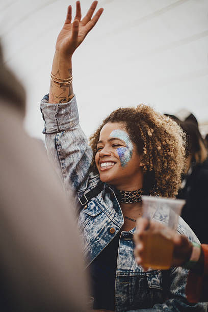 Hands In The Air Like You Don't Care Woman is dancing with her friends in a music marquee at a festival. She has glitter art on her face. glitter makeup stock pictures, royalty-free photos & images