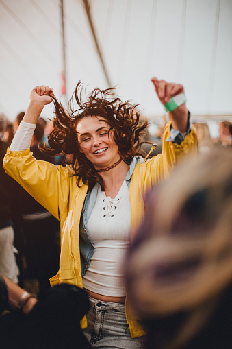 Young woman is dancing in a marquee at a music festival. She has her hands in the air and her hair is wild.