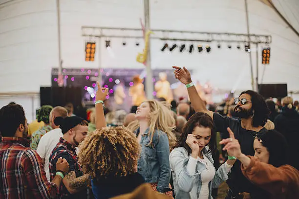 Group of friends dancing together in a marquee at an outdoor music festival.