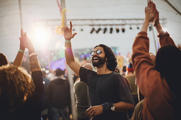 Festival Vibes People are dancing in a performance tent at a music festival. The main focus is on a man who is wearing sunglasses and is dancing with a hand in the air. real people photos stock pictures, royalty-free photos & images