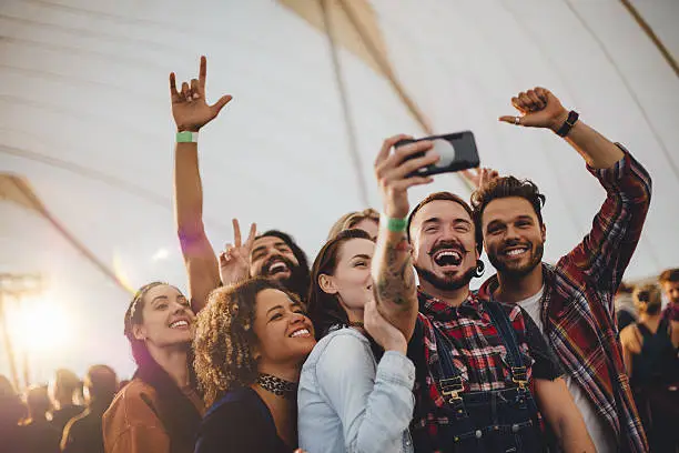 Group of young adult friends are taking a group selfie on a smartphone while they are at a festival.