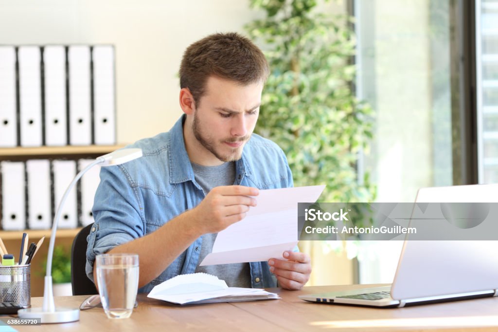 Serious entrepreneur reading a letter Serious entrepreneur working and reading a letter in a desktop at workplace Letter - Document Stock Photo