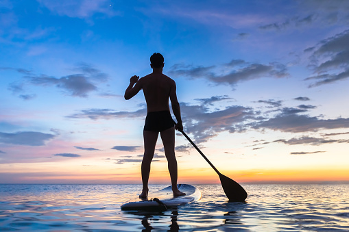 Silhouette of stand up paddle boarder paddling at sunset on a flat warm quiet sea