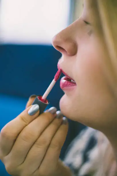 Photo of cute young girl putting red lipstick on lips