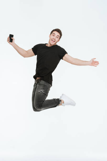 istock Happy young man jumping over white background holding phone. 638667152
