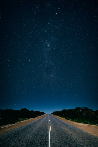 Composite of a Australian Outback road at night, with the sky overhead full of stars.