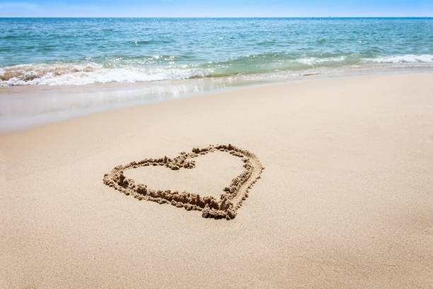 Heart drawn on a sandy beach. Children's bare feet. Sea waves.