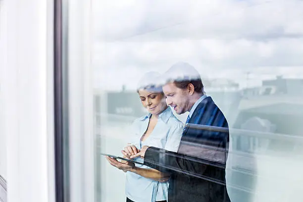 Business people standing behind glass wall using tablet computer