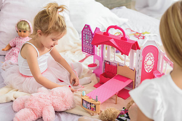 Carefree siblings playing in bedroom Pretty little child is enjoying game in doll house with her elder sister. She is sitting on bed and smiling girl playing with doll stock pictures, royalty-free photos & images