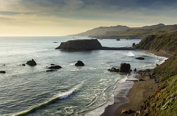 The sun beginning to set over the Pacific Ocean in a view looking down over Blind Beach and Goat Rock near Jenner in Sonoma County, Northern California.