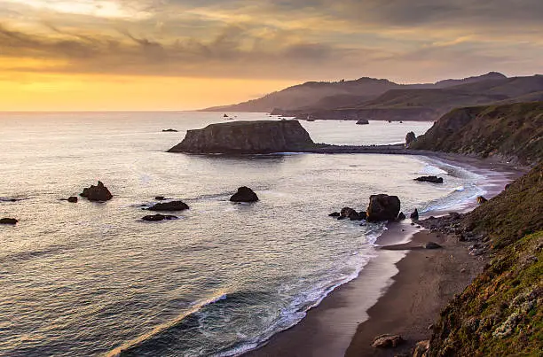 The sun beginning to set over the Pacific Ocean in a view looking down over Blind Beach and Goat Rock near Jenner in Sonoma County, Northern California.