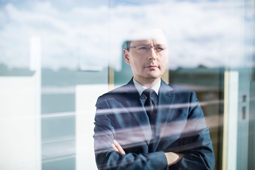 Thoughtful mature businessman standing behind glass
