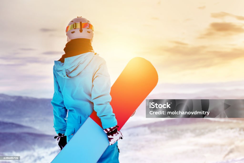 Snowboarder woman girl sunrise mountain top Girl snowboarder stands with snowboard on mountain's top on sunrise backdrop. Sheregesh ski resort Skiing Stock Photo