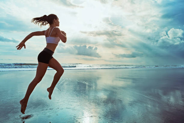 donna sportiva attiva corre lungo la spiaggia dell'oceano al tramonto. background sportivo. - one person beautiful barefoot beach foto e immagini stock