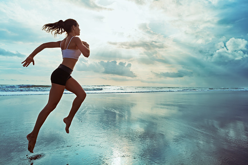 Active sporty woman run along sunset ocean beach. Sports background.