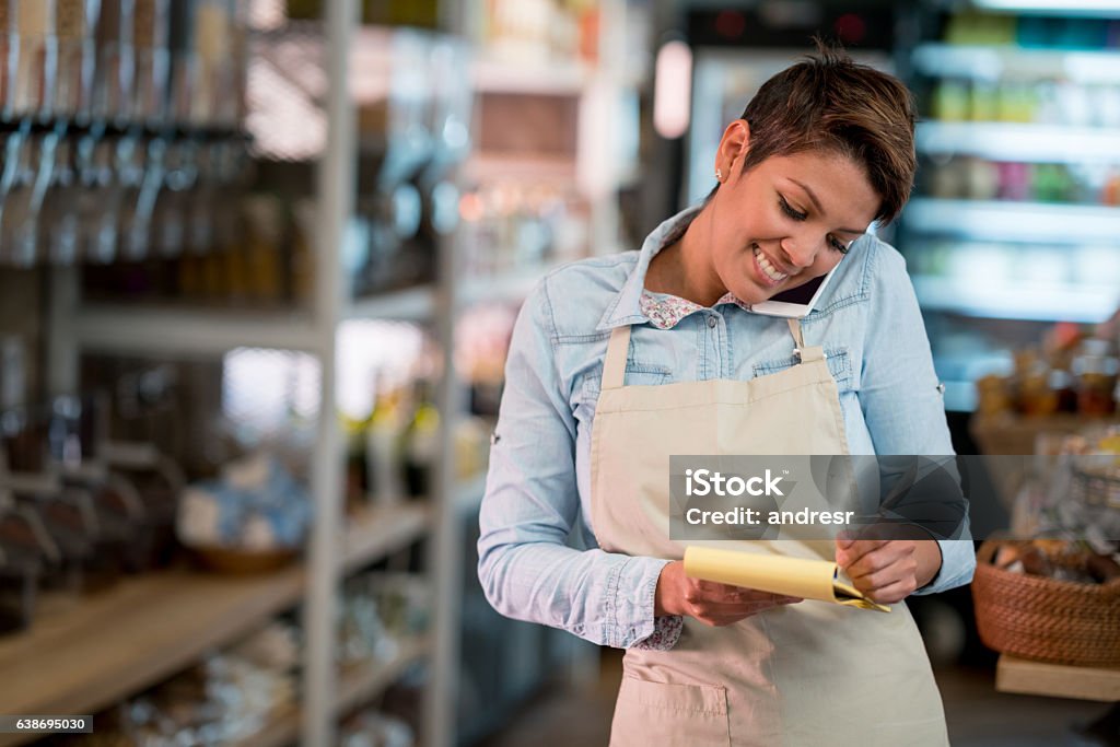 Woman at a grocery store talking on the phone Happy Latin American woman at a grocery store talking on the phone and taking a delivery order Delivering Stock Photo