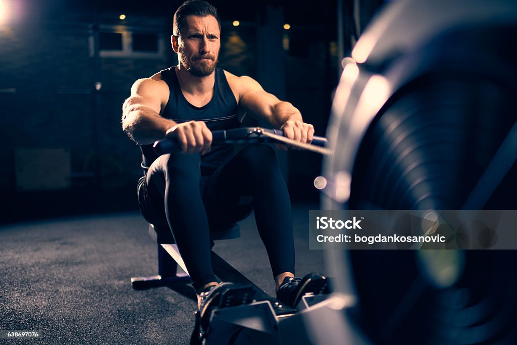 Rowing machine exercising Young man doing exercises on rowing machine in a gym. Rowing Machine Stock Photo